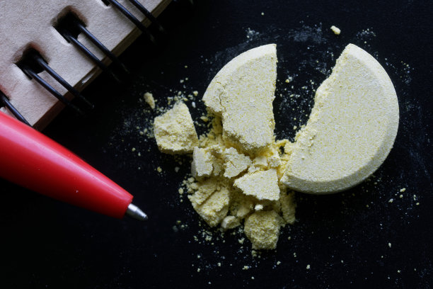 一个黄色的大药丸，分成两半，躺在黑色的背景上，旁边是一个笔记本和一支钢笔。宏图片下载