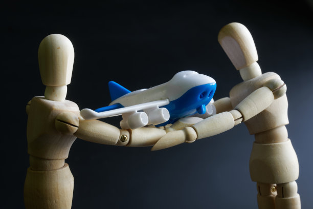 两个拟人模型正小心翼翼地拿着一架玩具客机。航空运输和客机安全概念。黑色背景图片下载