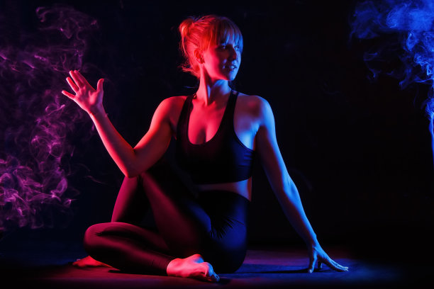 年轻女子做瑜伽体式。在黑色背景的红色霓虹灯和蓝色灯光下练习瑜伽。熏香的烟。图片下载