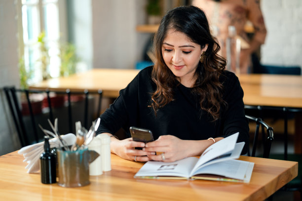 年轻女子在咖啡馆看书和使用手机。图片下载
