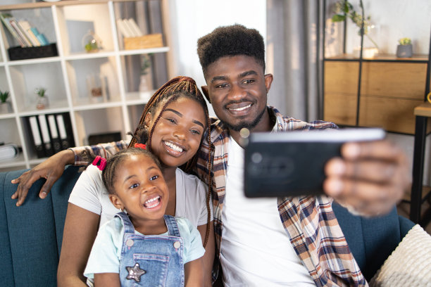 快乐的非洲家庭在沙发上休息时使用手机图片下载