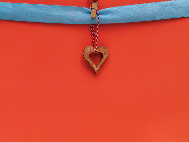 一颗木制的心挂在蓝色的丝带上，红色的背景上有一个晒衣夹。情人节作文。平铺，复制空间。贺卡。图片下载