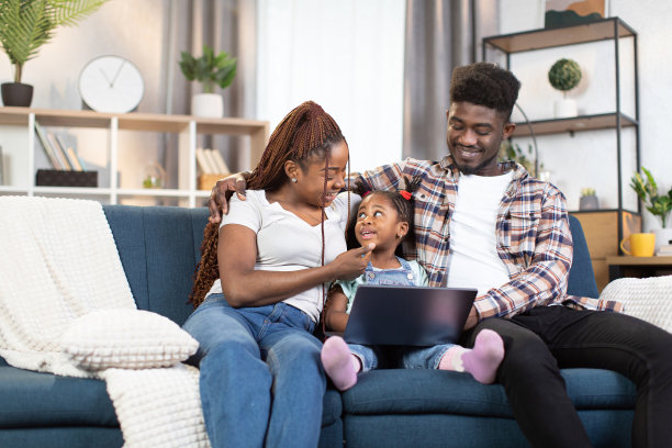 父母带着女儿坐在沙发上用现代笔记本电脑图片下载