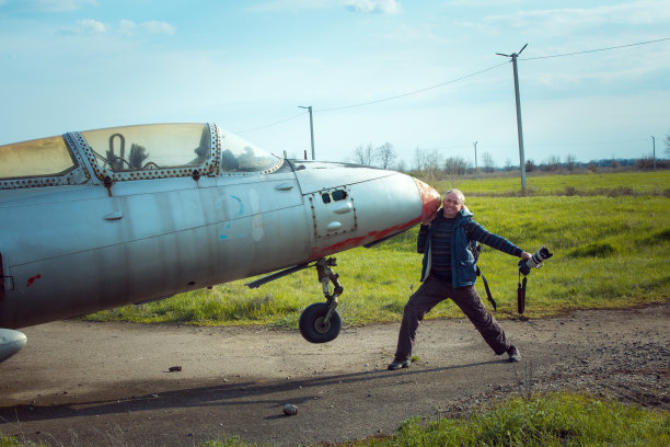 一个中年男子在一架废弃的旧苏联飞机旁。飞机在旧机场的场地上图片下载