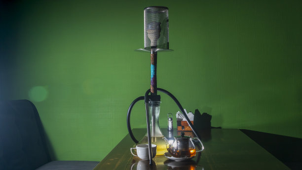 传统的阿拉伯水烟和带镜头光晕的茶。一壶茶和正在吸烟的水烟在深绿色的背景。图片下载