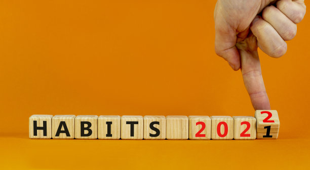 2022的习惯和新年的象征。商人转动木块，将“2021年习惯”改成“2022年习惯”。漂亮的橙色背景，复制空间。商业，2022年习惯和新年观念。图片下载