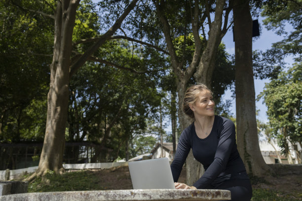 年轻人在白天使用智能手机，背景是一个绿色的公园。高质量的照片图片下载