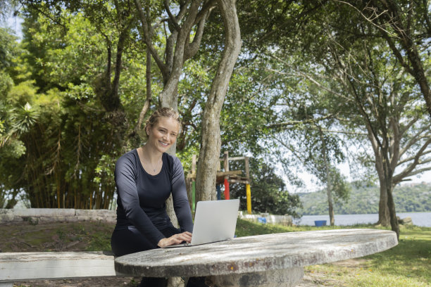 年轻人在白天使用智能手机，背景是一个绿色的公园。高质量的照片图片下载