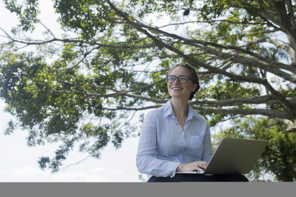 年轻人在白天使用智能手机，背景是一个绿色的公园。高质量的照片图片下载