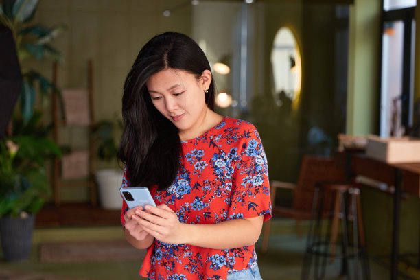 迷人的亚洲女性穿着橙色t恤在家里使用智能手机。开朗的女孩在社交网络上打字图片下载