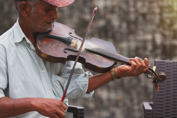 近距离的照片，一个老音乐家在户外，穿着脱光的衬衫，拿着小提琴，演奏美丽的旋律。图片下载