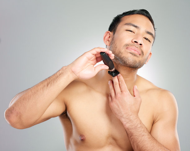 一个英俊的年轻人在灰色的背景下刮胡子图片下载