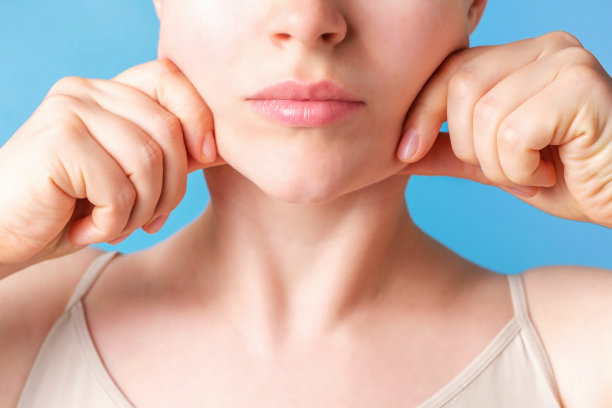 女性的手在蓝色背景上做脸部特写的自我按摩。图片下载