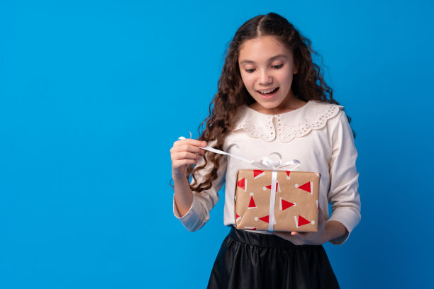 快乐的长发小女孩，拿着一个蓝色背景的礼品盒图片下载