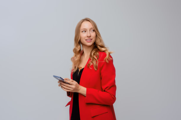 成功的年轻女企业家的肖像，她的手拿着手机，微笑着，高兴地看着一边，站在灰色的背景图片下载