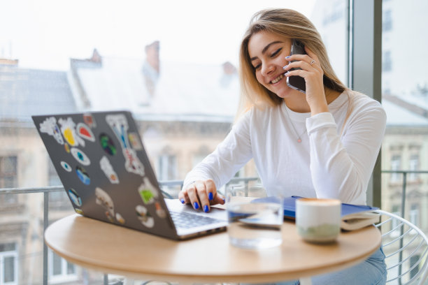 微笑的年轻女孩在咖啡馆聊天，同时在笔记本电脑上工作图片下载