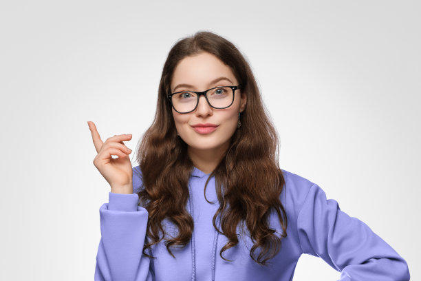 一个留着长发，戴着眼镜，面带微笑的少女。女孩穿着一件紫色的超大号运动衫，向上指着。图片下载