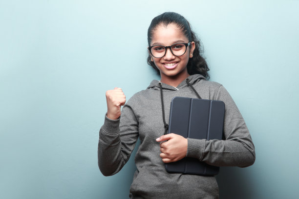 这是一幅印度裔女孩的肖像，她面带微笑，手里拿着一部平板电脑，并摆出一个欢呼的姿势图片下载