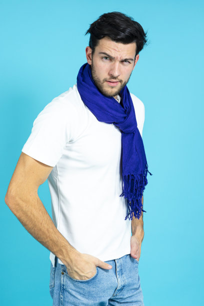 白种人帅哥戴着深蓝色围巾摆姿势，穿着白色衬衫，直视蓝色背景下的相机图片下载