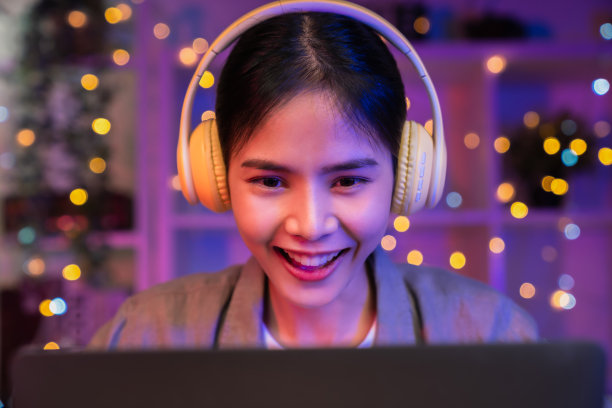 年轻的亚洲女性带着幸福的微笑，在房子里用黄色耳机和手提电脑听着音乐。图片下载