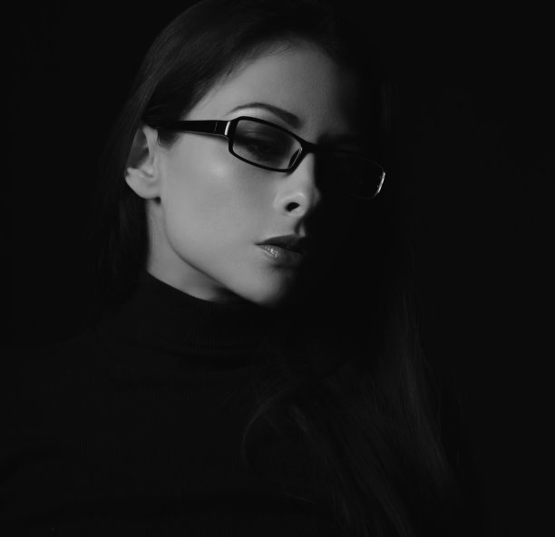 商业思维的女人，戴着时尚的眼镜，在黑暗的阴影背景下看着黑色的衣服。特写侧面视图人脸肖像。黑色和白色图片下载