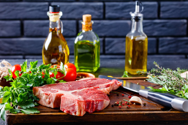 上等腰牛排配香草，香料。牛排放在质朴的木板上，背景是酒瓶和砖墙图片下载
