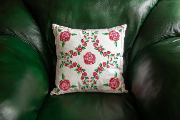 手工装饰枕头与玫瑰刺绣在绿色皮革沙发。图片下载