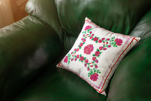 手工装饰枕头与玫瑰刺绣在绿色皮革沙发。图片下载