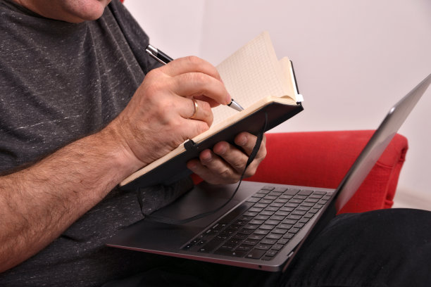 一个男人把笔记本电脑放在膝盖上，在笔记本上做笔记，特写，在线商业分析图片下载