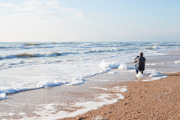 冬天的一天，一名男子在沙滩上用手机拍摄海景照片图片下载