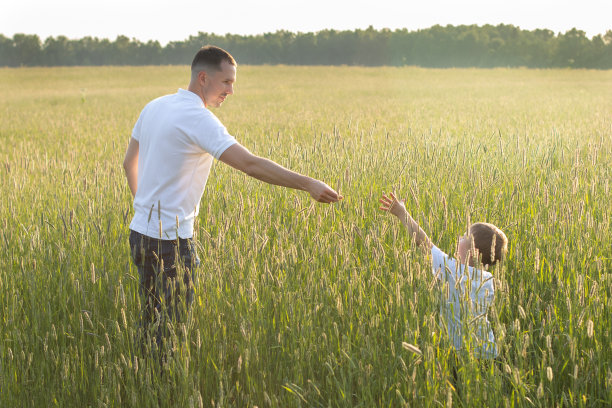 日落时分，父子俩在田野里。父亲向儿子伸出手。幸福的家庭的概念。图片下载