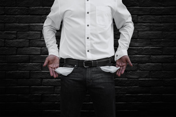 一个男人在黑色的砖墙背景上展示他的空口袋。图片下载