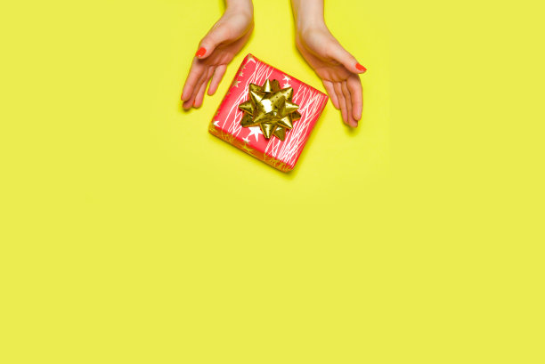 美丽的红色礼盒与蝴蝶结在妇女的手中，黄色的背景，俯视图，为文本的地方。图片下载