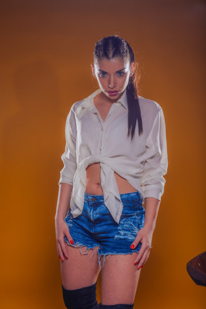 一名年轻女子穿着时尚的服装，白色亚麻衬衫和蓝色短裤牛仔裤在工作室里单独摆姿势图片下载