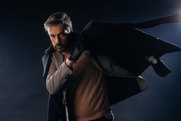 一名穿着正式、头发灰白的英俊成年男子在黑色背景的工作室里摆姿势的肖像。图片下载