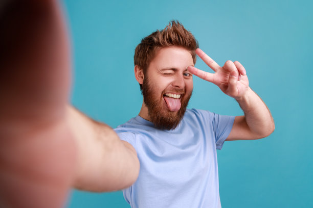 一个人在自拍，看着相机的视角，照片的角度，露出胜利的手势，伸出舌头图片下载