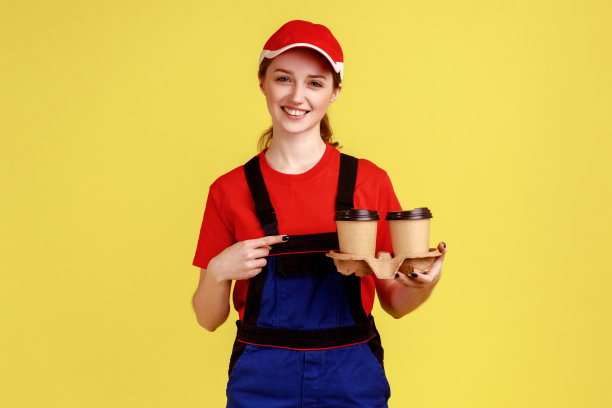 正面带微笑的快递女站着，指着咖啡杯，微笑着看着镜头。图片下载