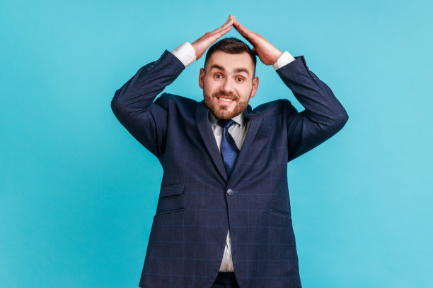 我很安全！友善的男人穿着正式的西装，头顶做出屋顶手势，面带微笑，感到安全，梦想着房子图片下载