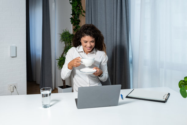 年轻快乐成功的女企业主在办公室用笔记本电脑工作时喝杯咖啡休息。女企业家，自信的女士，喝着热饮在电脑上阅读电子邮件图片下载