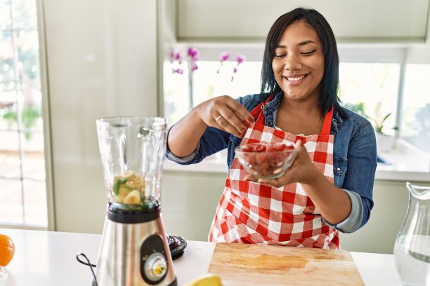 西班牙黑发女人准备水果奶昔与树莓在厨房图片下载