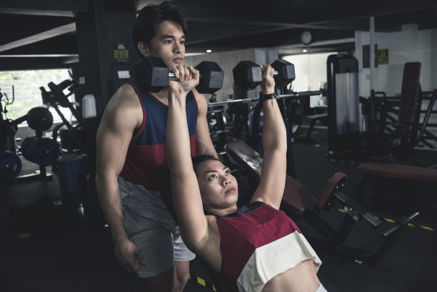 一个年轻的亚洲男子看到一个运动女孩在做倾斜的哑铃按压。在健身房的帮助下锻炼。图片下载