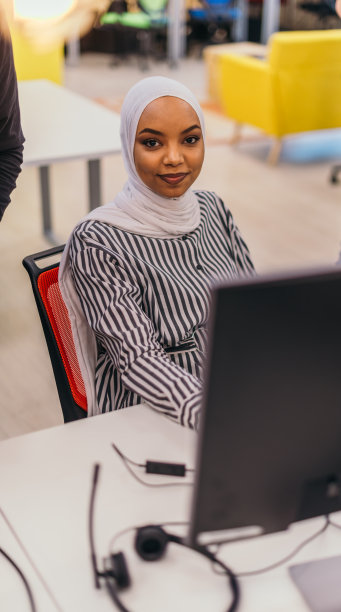 一个美丽的非洲女孩的肖像穿着希贾布，坐在她的电脑前工作。图片下载