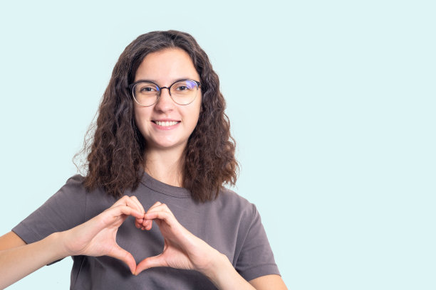 快乐的女孩戴着眼镜，卷着头发，把手做成心形。女孩感恩，感恩，露出心迹图片下载