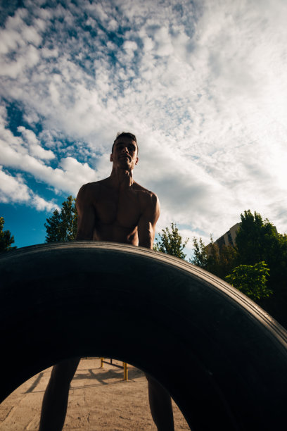 一个穿着运动服的裸上身男子在蓝天下的健身房里翻转轮胎图片下载