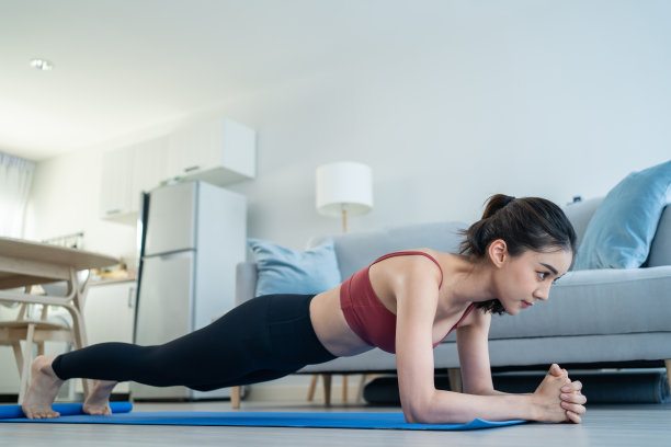 亚洲美丽的年轻女子呆在家里，做有氧运动在家里。有吸引力的女孩做锁定活动锻炼地板上的平板跟随指导视频从在线教练的健康在房子图片下载