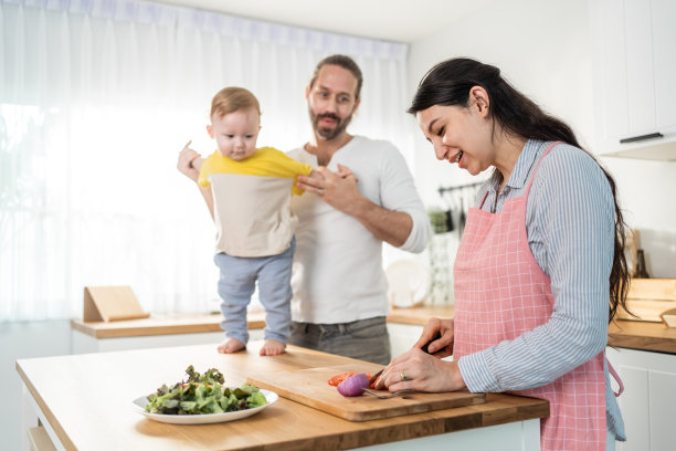 白种人漂亮的父母和小男孩在厨房做饭。幸福的家庭，年轻漂亮的母亲做健康的沙拉作为午餐，而丈夫和父亲抱着小宝宝在房子里图片下载