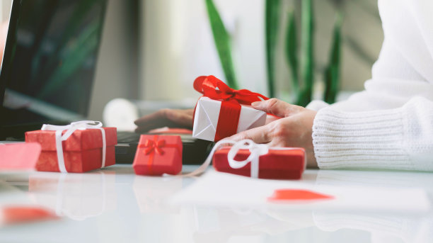女人手里拿着信用卡和礼物，对着笔记本电脑。在线购物。情人节礼物。2月14日关于COVID-19大流行。送货上门。节假日网购。隔离图片下载