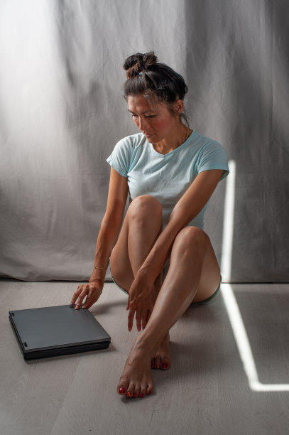 一个穿着短裤的年轻女子坐在地板上看着她旁边的笔记本电脑图片下载