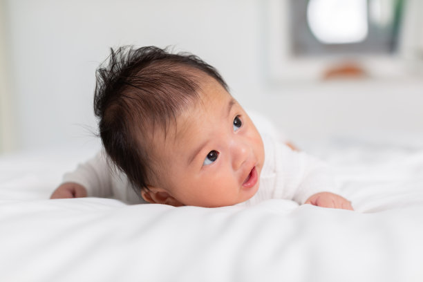 新生儿3个月俯卧，发育颈部控制能力，加强颈部和肩部肌肉。可爱的婴儿躺在白色的床上爬行，快乐而有趣。肚子上的时间的概念图片下载