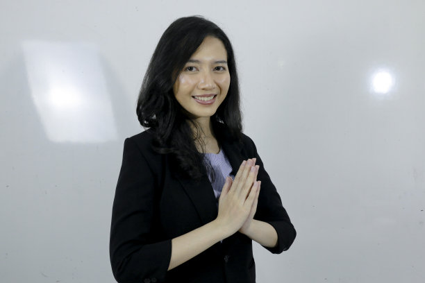 商业年轻的亚洲女孩给问候的手在她的脸上一个大大的微笑。灰色背景的印度尼西亚女人。图片下载